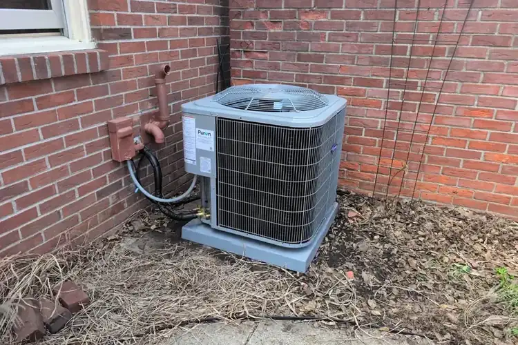 A Carrier AC condenser fitted by Hinding Heating against a brick wall